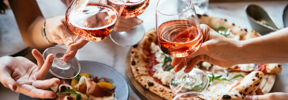 Friends enjoy a dinner party with pizza and rose wine in a bar or a restaurant.