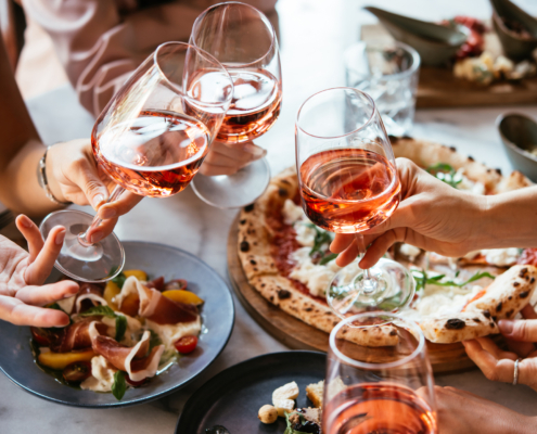 Friends enjoy a dinner party with pizza and rose wine in a bar or a restaurant.